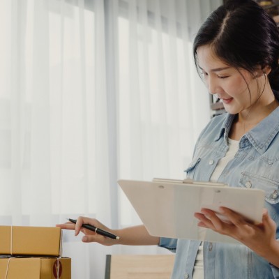 Beautiful smart Asian young entrepreneur business woman owner of SME checking product on stock and write on clipboard working at home. Small business owner at home office concept.