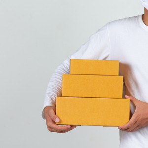 A man wearing a white t-shirt is holding a brown post box to deliver things Make gestures and facial expressions.